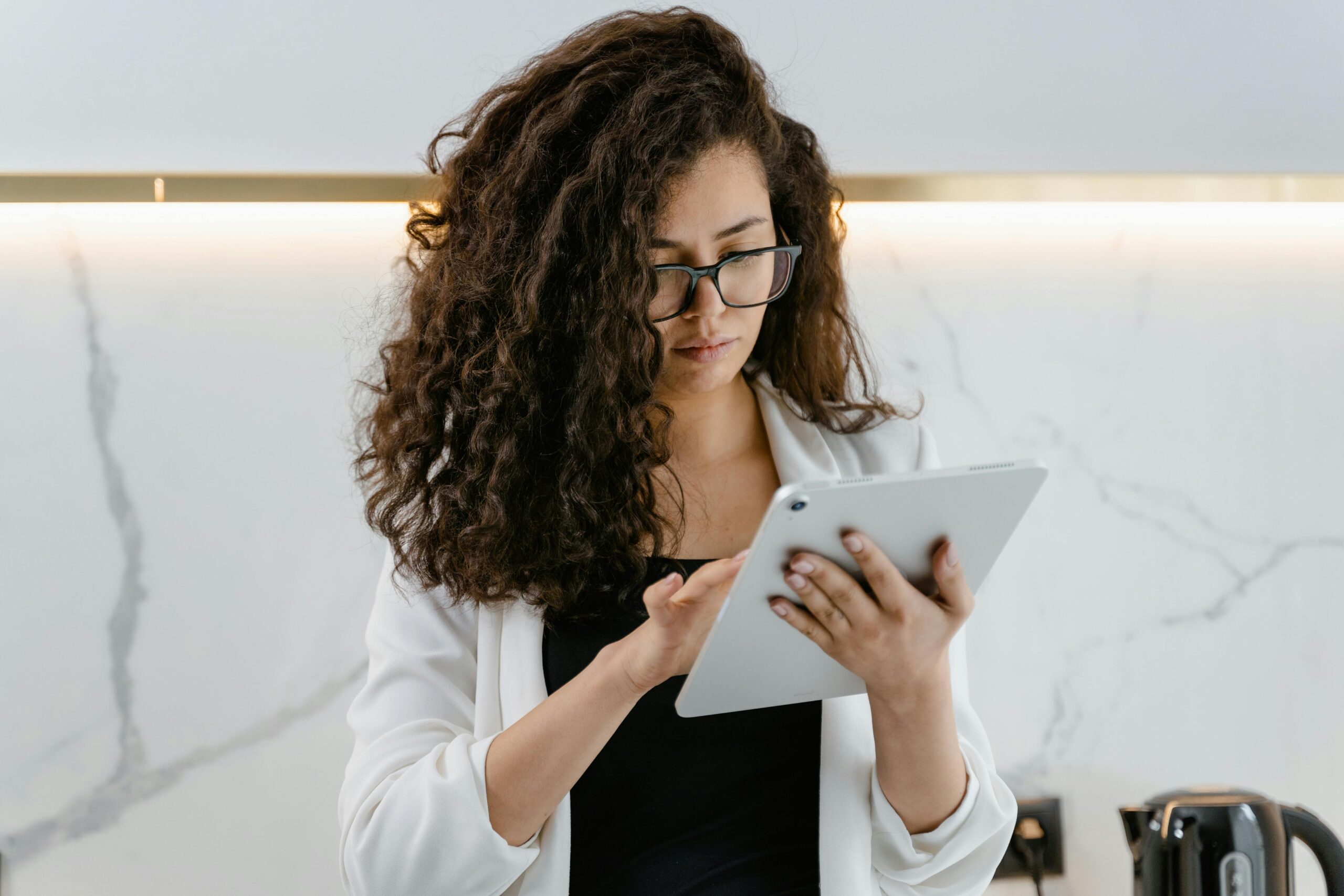 A woman uses a tablet in a modern kitchen, focusing on technology and multitasking.